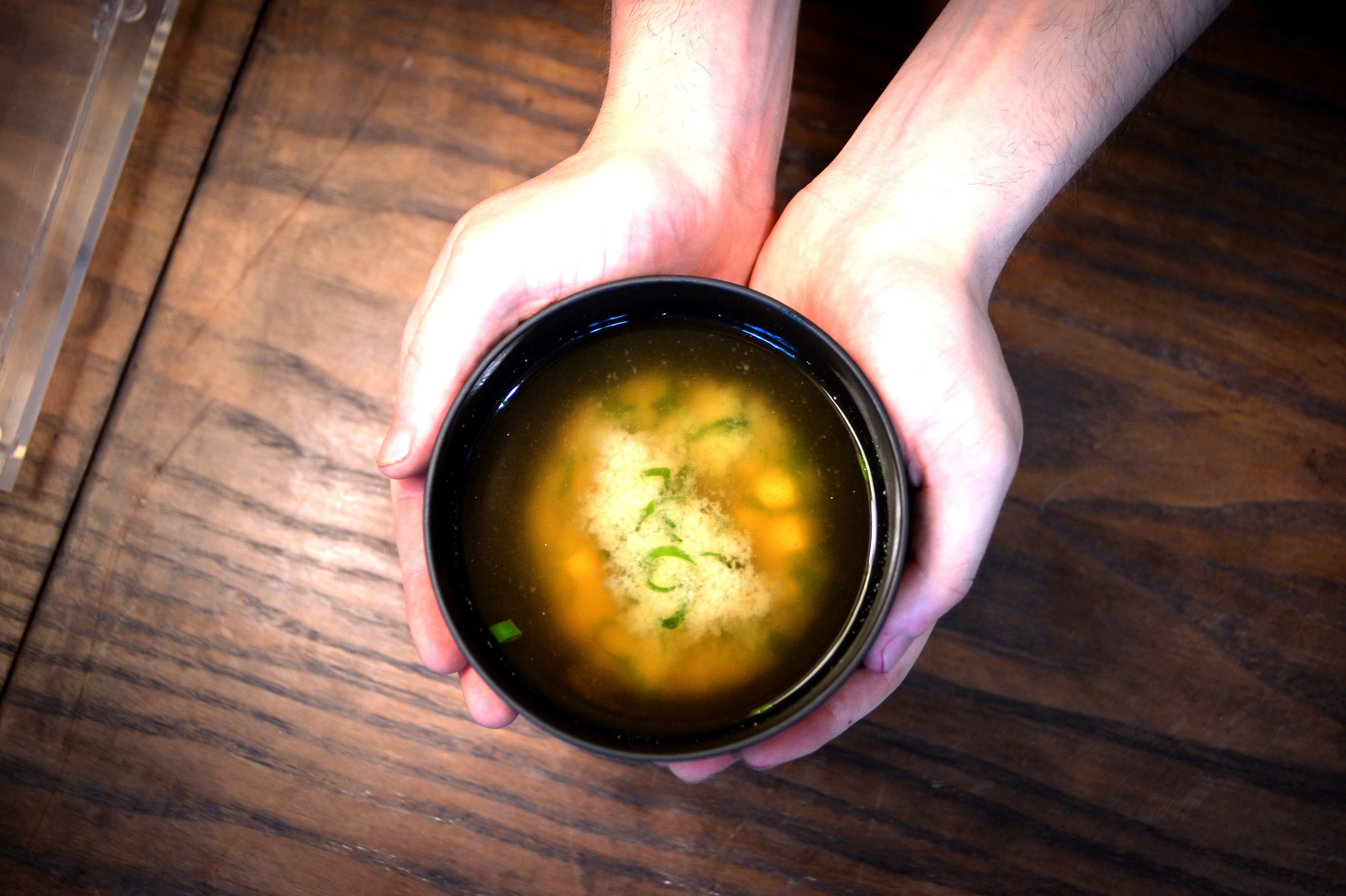 Hands cradling a black bowl of broth