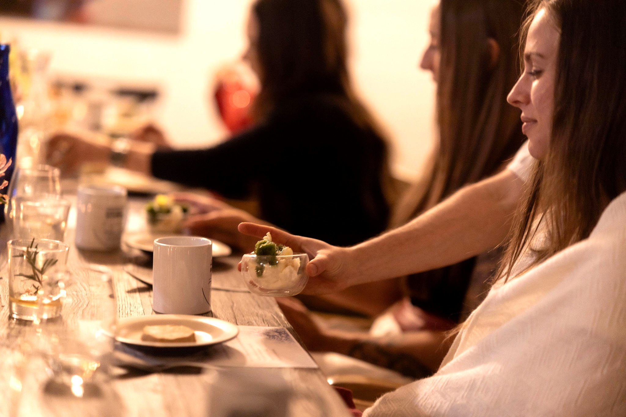 Woman passing a small white bowl down a candlelit dinner table